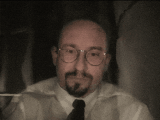 a man with glasses and a beard wears a white shirt and tie