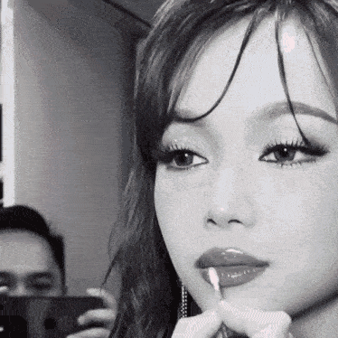 a woman is applying lipstick while a man takes a picture of her