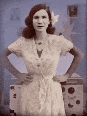 a woman in a white dress with a flower in her hair stands with her hands on her hips