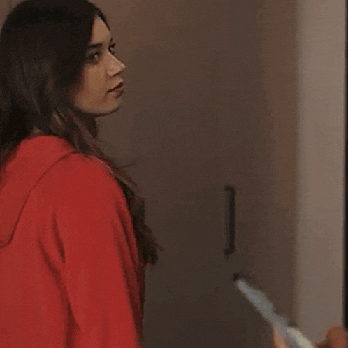 a woman in a red hoodie is standing in a room holding a broom and giving a thumbs up .