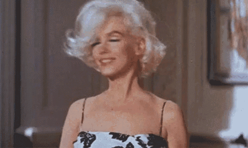 a woman with blonde hair is standing in a room wearing a white and black dress .