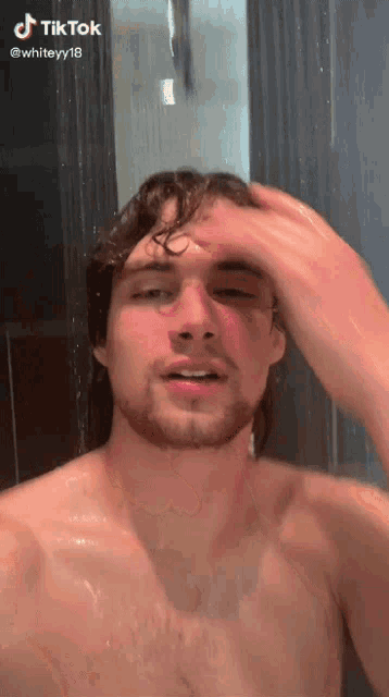 a shirtless man with a beard is taking a shower in a bathroom