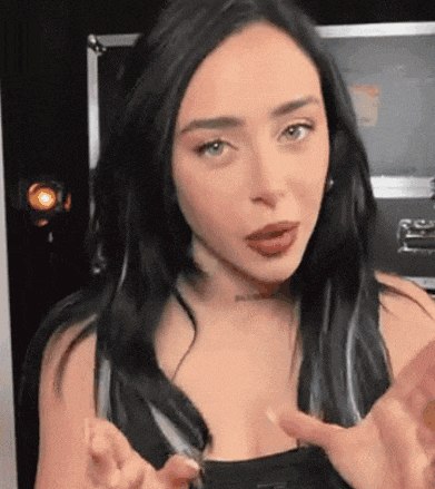 a woman with long black hair is making a funny face and pointing at something .