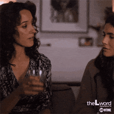 two women are sitting on a couch and one is holding a glass of water
