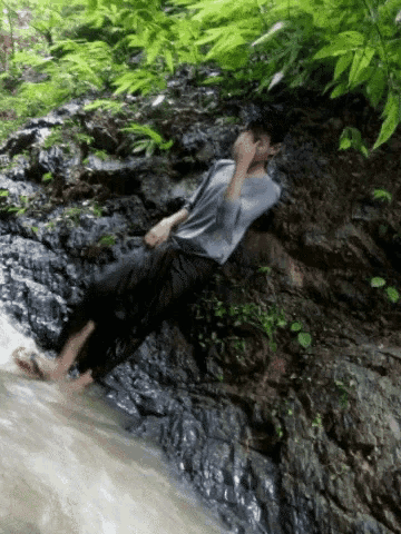 a man sits on a rock near a waterfall with his feet in the water