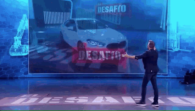 a man stands on a stage in front of a large screen that says el desafio