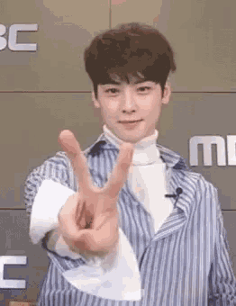 a young man in a striped shirt is making a peace sign with his fingers .