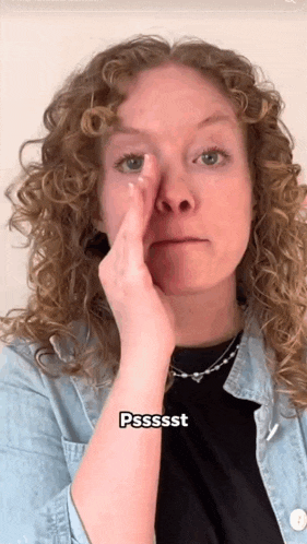 a woman with curly hair holds her hand to her nose and says pssssst
