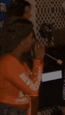 a woman in an orange shirt is sitting in front of a television screen .