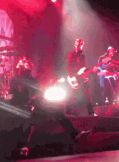 a group of people are playing instruments on a stage in a dark room with red lights .