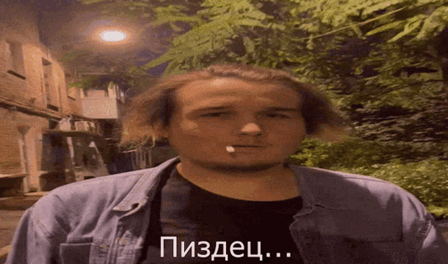 a man with a cigarette in his mouth is wearing a denim jacket and a black shirt