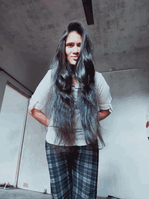 a woman with very long black hair wearing plaid pants and a white shirt