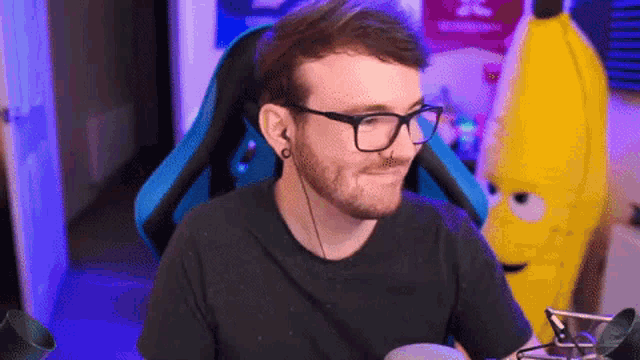 a man wearing glasses and ear buds is sitting in front of a yellow stuffed banana