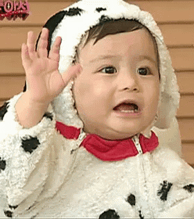 a baby wearing a dalmatian costume is waving his hand .