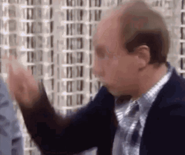 a bald man in a suit and tie is making a funny face with his hands .