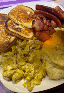a white plate topped with pancakes scrambled eggs bacon and cheese