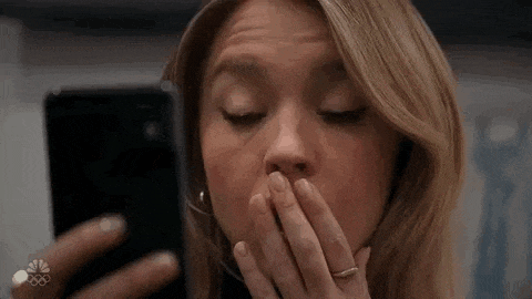 a woman is covering her mouth with her hand while looking at her phone .