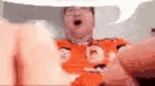 a man in an orange shirt is holding a teddy bear in his hand .