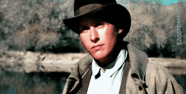 a man wearing a cowboy hat is standing in front of a body of water ..