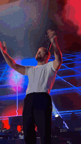 a man with a beard is singing into a microphone on a stage with his arms outstretched .