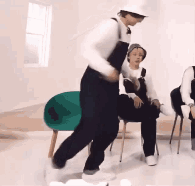 a man in overalls and a hard hat is dancing in a room with other people .