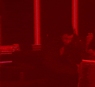 a person is standing in a dark room with red lights behind them and a statue of a city in the background .