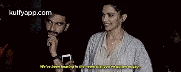 a man and a woman are standing next to each other and the woman is holding a cell phone .