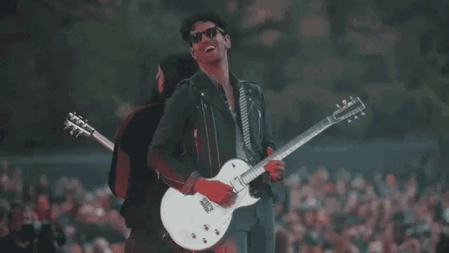 a man in a leather jacket is playing a white guitar on stage .