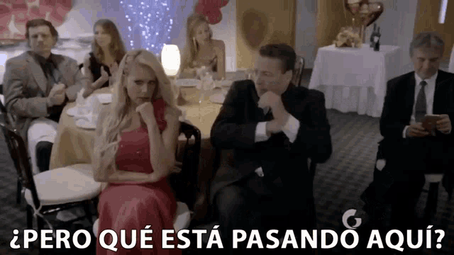 a woman in a red dress sits next to a man in a suit with the words pero que esta pasando aqui written below her