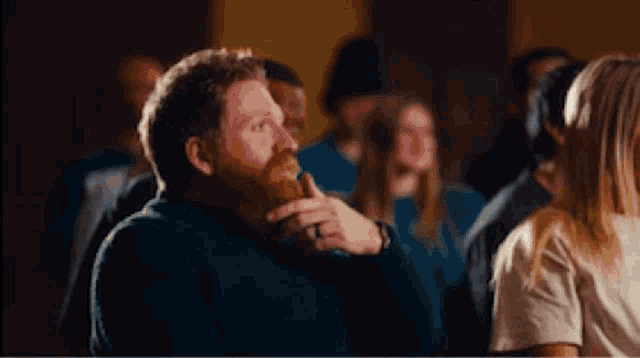 a man with a beard is eating a sandwich in a crowded room .