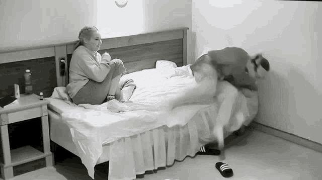 a black and white photo of a woman sitting on a bed with a man standing on it .
