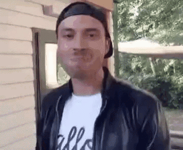a man wearing a leather jacket and a baseball cap is making a funny face .