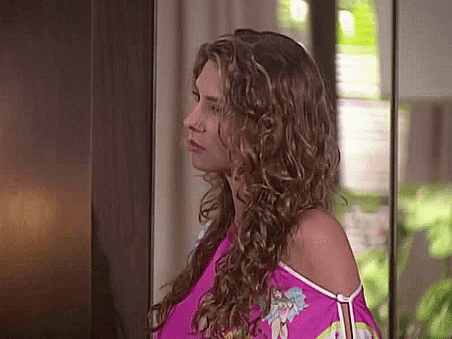 a woman with curly hair is standing in front of a mirror and looking at herself .