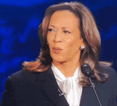 a woman in a suit is speaking into a microphone and making a funny face