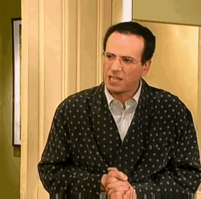 a man in a polka dot robe and glasses is standing in front of a door .