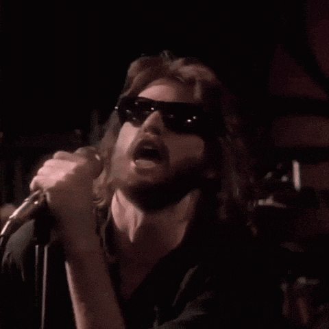 a man is singing into a microphone while wearing sunglasses in front of a crowd .