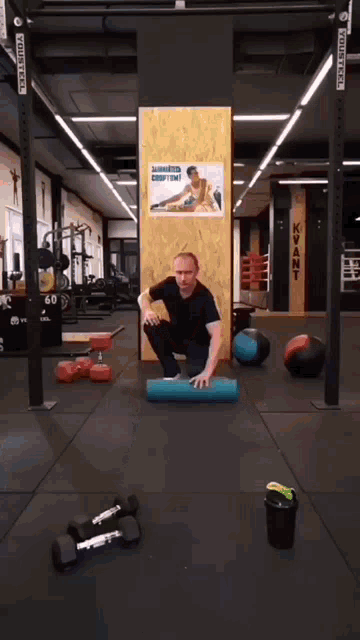 a man is squatting on a blue foam roller in a gym with a poster on the wall that says " bodytec "