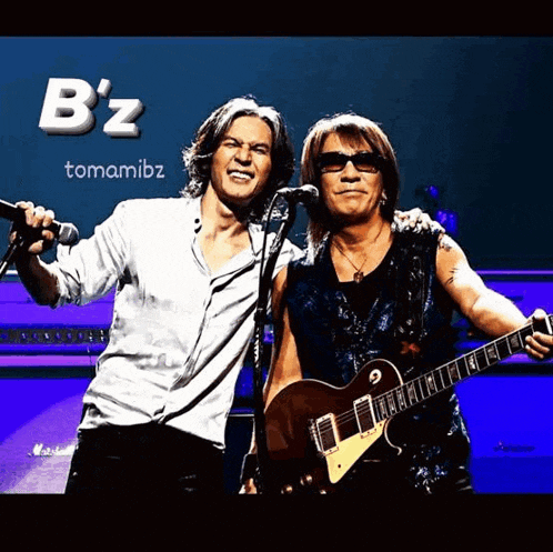 two men are standing next to each other and one is holding a guitar while the other sings into a microphone
