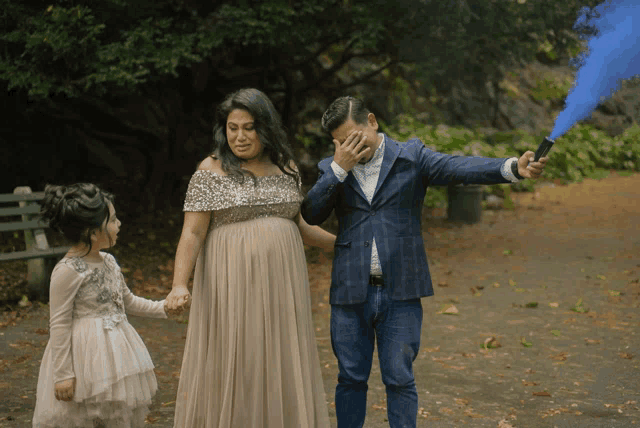 a man is covering his face while holding a blue smoke bomb while standing next to a pregnant woman and a little girl