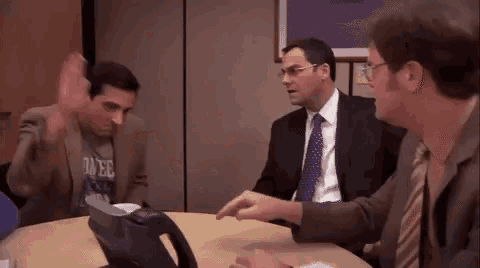 a group of men are sitting around a table talking to each other in an office .