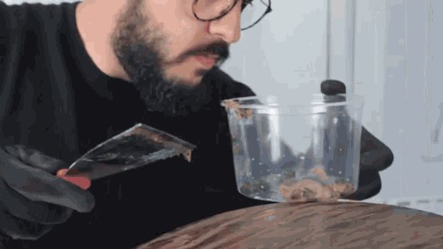 a man holding a spatula next to a plastic cup filled with bugs
