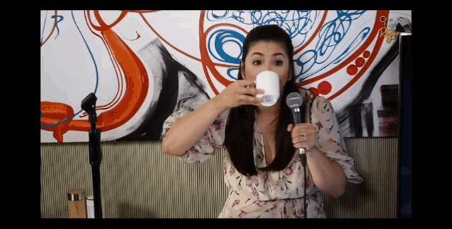 a woman is drinking from a white cup in front of a microphone