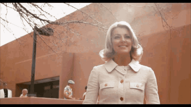 a woman in a white jacket is smiling in front of a brown building
