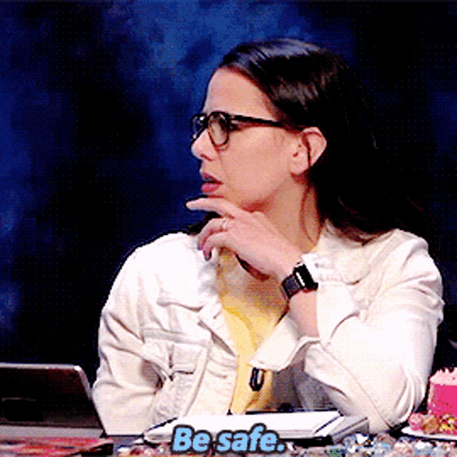 a woman wearing glasses sits at a desk with a sign that says be safe