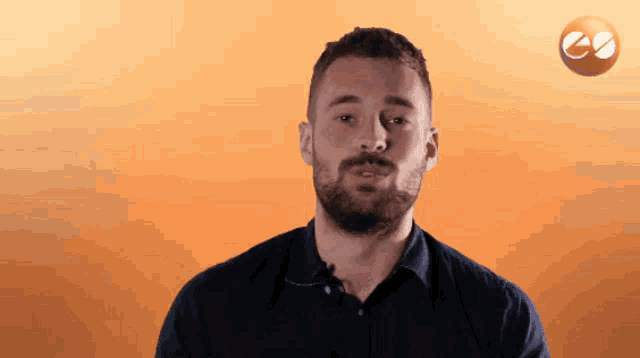 a man with a beard stands in front of an orange background with a circle with the letter e on it