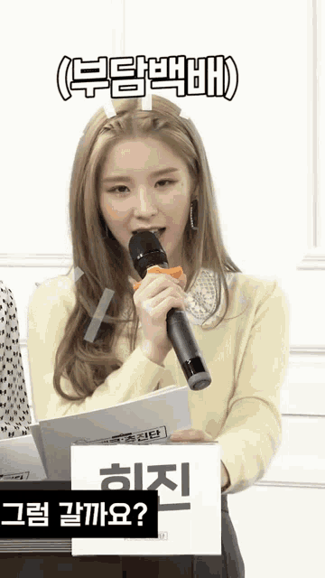a woman in a yellow sweater is holding a microphone and a box with chinese writing on it .