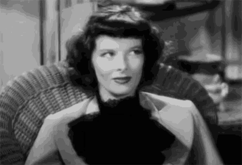 a black and white photo of a woman sitting in a wicker chair looking up .
