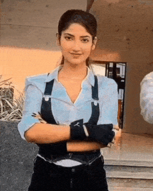 a woman in a white shirt and black overalls with her arms crossed .