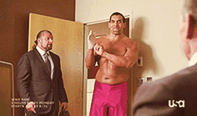 a shirtless man in pink shorts is standing next to a man in a suit and tie