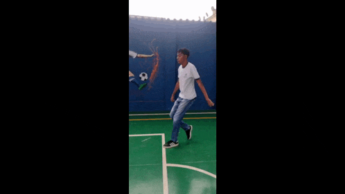 a man in a white shirt and jeans is standing on a green basketball court .